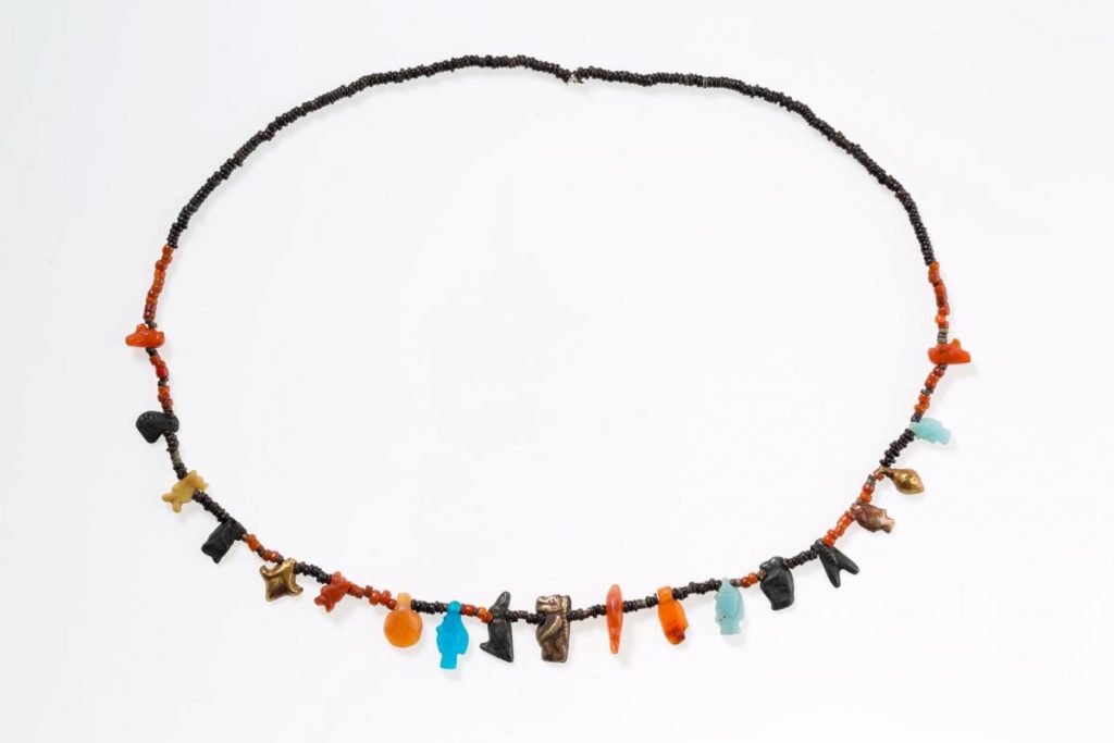 Ancient Egyptian Jewelry Necklace with disc beads and amulets from the New Kingdom. This necklace is composed of tiny disk beads interspersed with a variety of amulets, including falcons, a frog, Tawerets, a lotus, bolti fish, a shell or bullae, a hand, and a "nefer" sign. Some amulets, such as the lotus, frog, and fish, symbolize fertility, while Taweret and the falcon offer protection. The "nefer" hieroglyph conveys a good wish. This necklace was one of three stored in a small jewelry box in a man's burial. Carnelian, gold, silver, faience, glass, yellow stone, tin